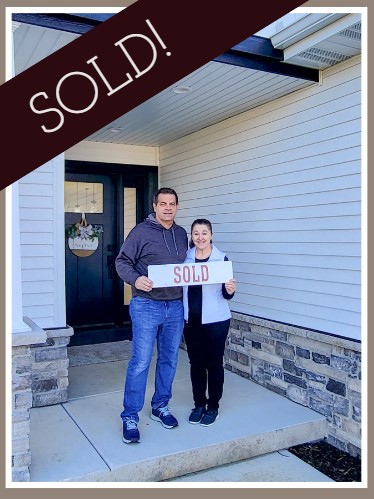 Couple holding a SOLD sign outside of a house